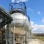 A large round ball-shaped shiny metallic high-pressure iron storage tank for ammonia is strong with pipes and equipment at the petrochemical chemical refinery industrial refinery.